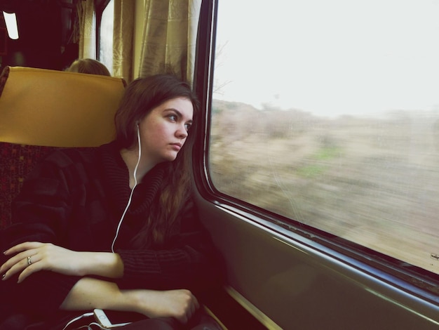 列車で旅している間音楽を聴いている考え深い女性