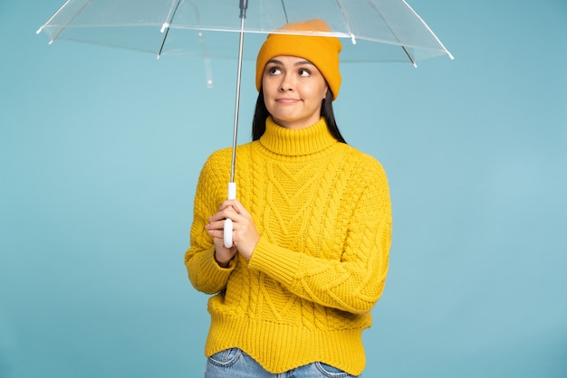 Thoughtful woman looks up at empty space for your ad,\
advertising. female person holding an umbrella from rain standing\
at isolated texture wall in studio