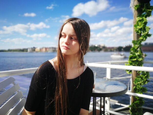 Photo thoughtful woman sitting on chair against sea at restaurant during sunny day