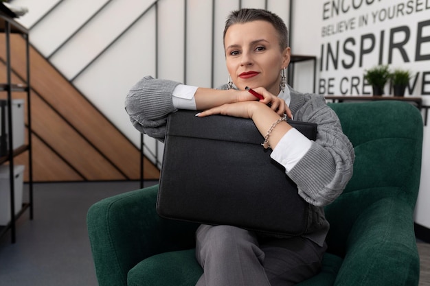 Thoughtful woman sitting in an easy chair in the office with a folder for documents in her hands