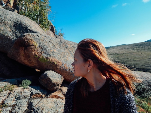 写真 空の向こうの岩の上に座っている思慮深い女性