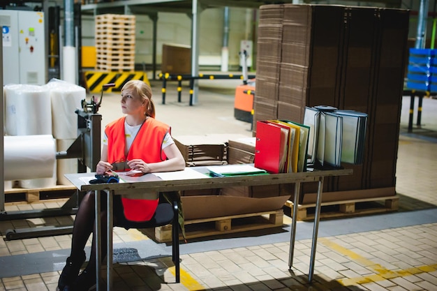 Photo thoughtful woman sitting at table in factory