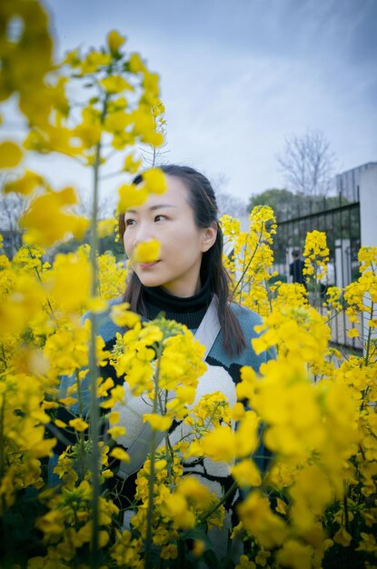 Thoughtful woman standing amidst yellow flowers against sky