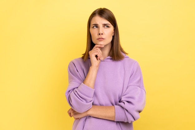 Thoughtful woman standing holding chin looking away thinks about something important