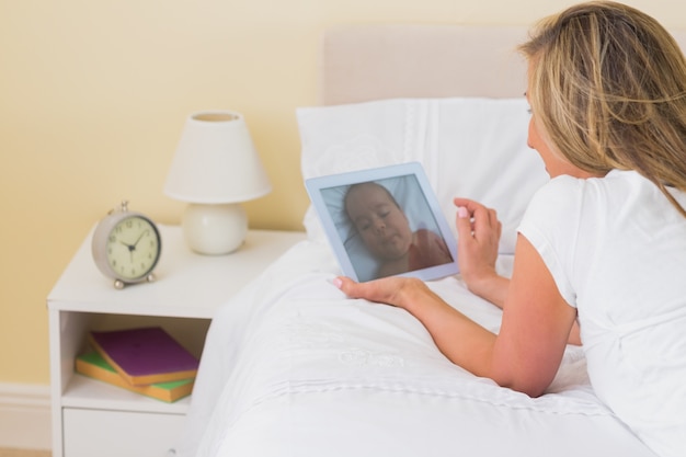 Задумчивая женщина, используя планшетный ПК, лежащий на кровати