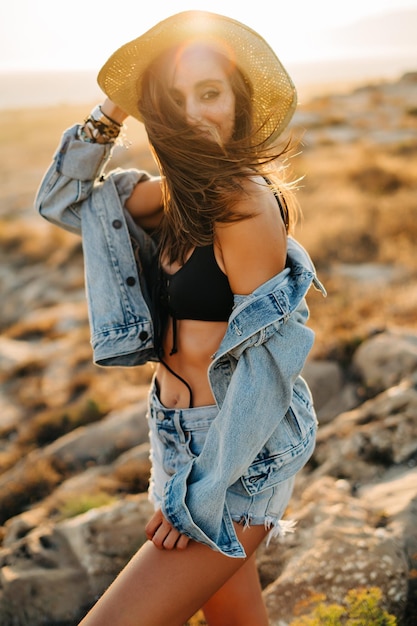 thoughtful woman wearing hat while standing at beach during sunset