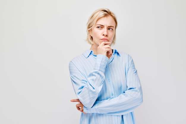 Thoughtful woman with hand on chin wearing a blue shirt isolated on a light background