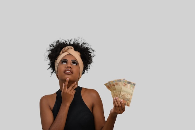 thoughtful woman with money, young afro woman with brazilian money, advertising concept on gray back