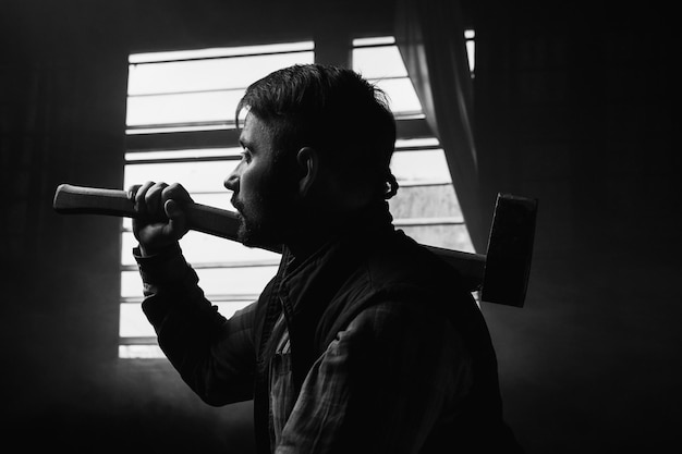 Thoughtful woodsman with axe focus on foreground. Pensive lumberjack in dark room, hard craftsmanship work, male strength background