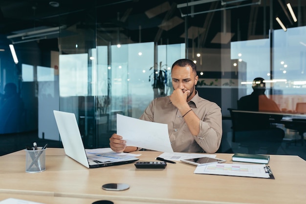 Thoughtful young africanamerican male designer architect sitting in the office at the table with a