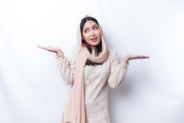 A thoughtful young Asian Muslim woman is wearing hijab and looks confused between choices isolated by a white background