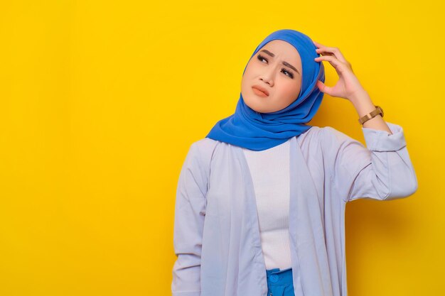 Thoughtful young asian muslim woman looking up at copy space\
thinking and making decisions isolated on yellow background