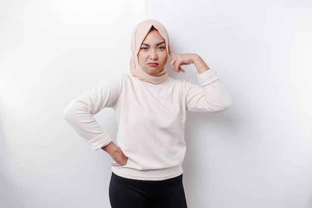 A thoughtful young Asian Muslim woman wearing headscarf while looking aside isolated by a white background