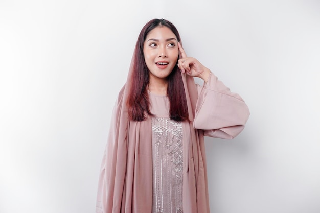 A thoughtful young Asian Muslim woman wearing headscarf while looking aside isolated by a white background