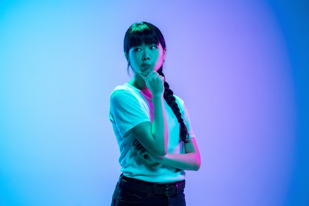 Thoughtful. Young asian woman's portrait on gradient blue-purple studio background in neon light. Concept of youth, human emotions, facial expression, sales, ad. Beautiful brunette model.