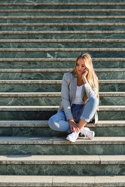 Thoughtful young blonde woman sitting on urban steps.