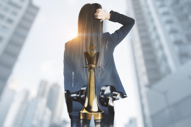 Thoughtful young businesswoman standing on blurry city background with mock up place and chess king Success strategy think future and ceo concept Double exposure