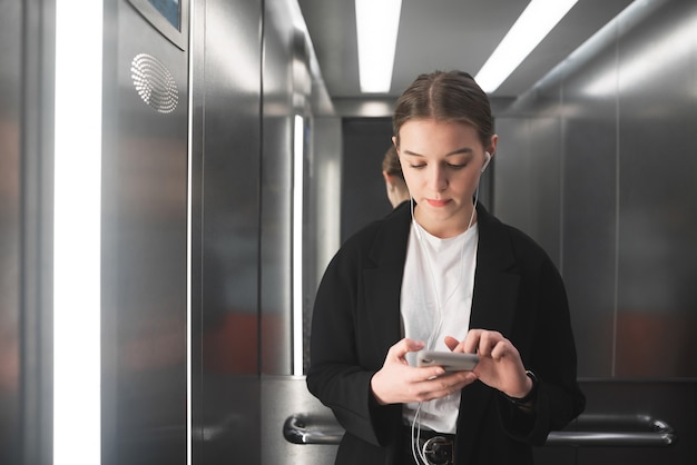 Thoughtful young female office worker is using her smartphone