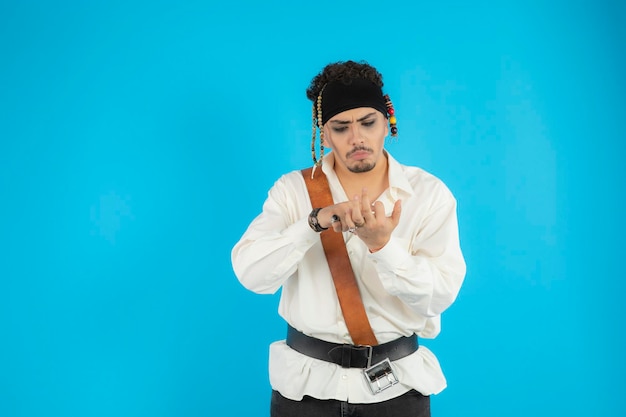 Thoughtful young handsome pirate looking at his hand on the blue background. High quality photo