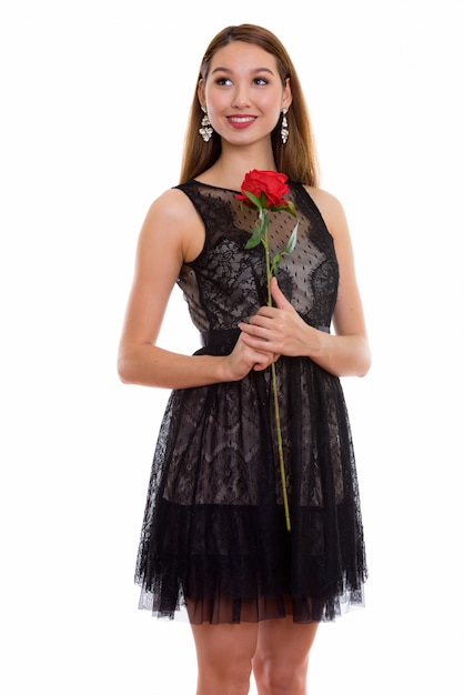 Foto riflessivo giovane bella donna asiatica felice sorridente e in piedi mentre si tiene la rosa rossa