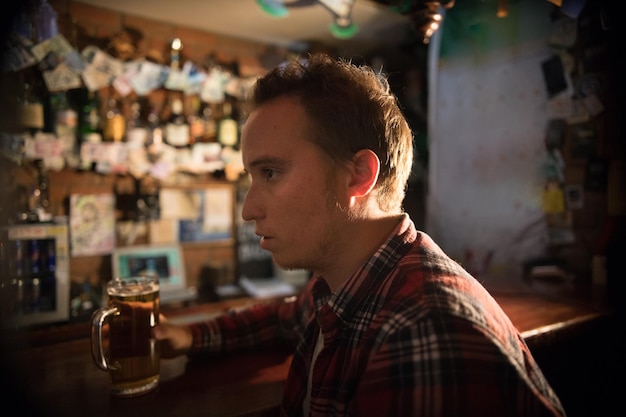 Thoughtful young man at the bar holding a pint of beer