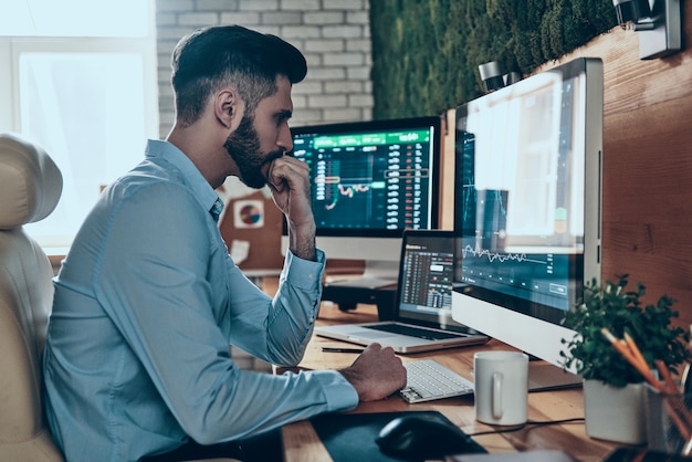 Thoughtful young man in formalwear working using computer while sitting in the office