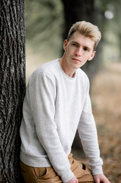 Photo thoughtful young man leaning on tree trunk in forest