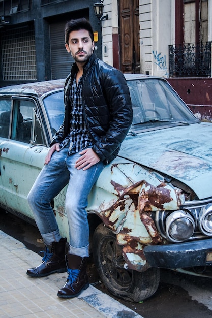 Foto giovane premuroso che guarda lontano mentre è seduto su un'auto abbandonata