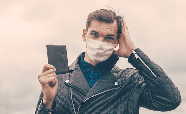 Thoughtful young man in a protective mask holds his passport