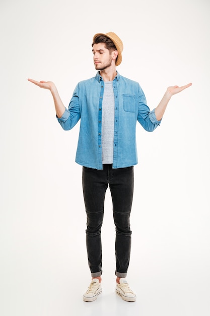 Thoughtful young man standing and holding copyspace on both palms over white background