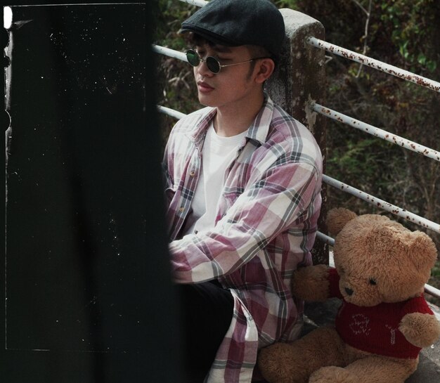 Photo thoughtful young man with teddy bear sitting on footbridge