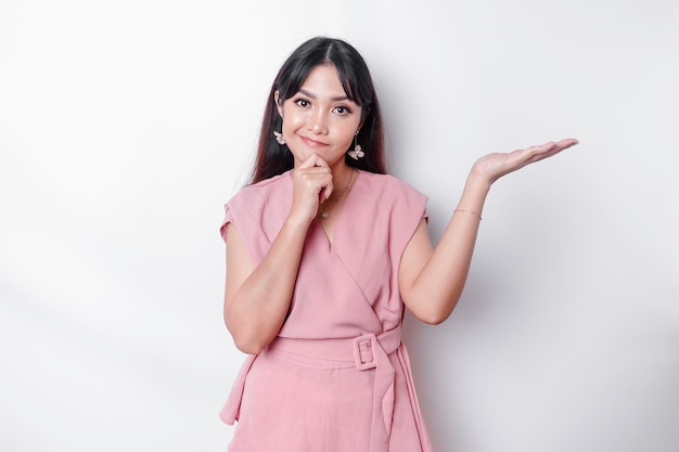 A thoughtful young woman dressed in pink and holding her chin while pointing copy space beside her isolated by white background