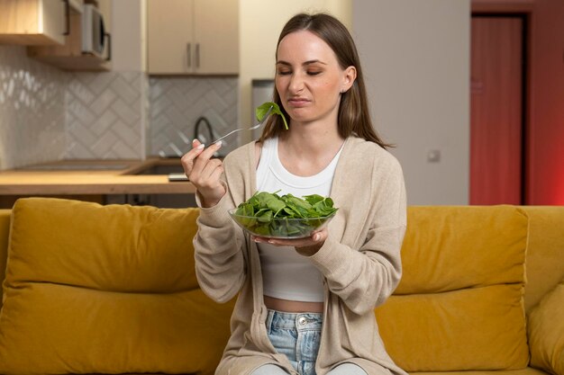 Photo a thoughtful young woman is eating a salad and experiencing a lack of appetite while sitting on the couch digestive problems as well as spoiled and tasteless food