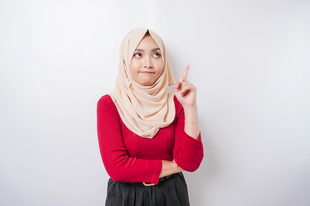 A thoughtful young woman is wearing a hijab and holding her chin isolated by white background