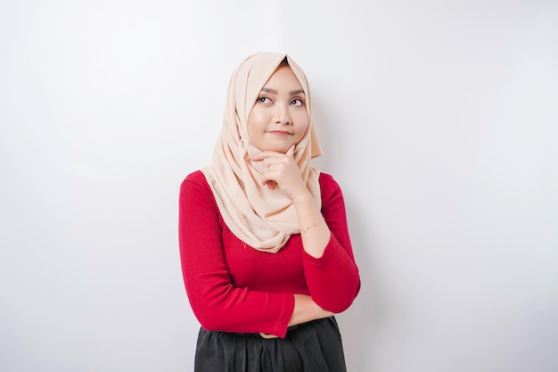 A thoughtful young woman is wearing a hijab and holding her chin isolated by white background