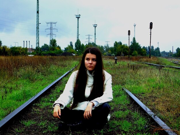 Thoughtful young woman looking away while sitting on grassy railroad track