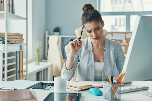 オフィスのテーブルに座ってスマートカジュアルな服装で思いやりのある若い女性