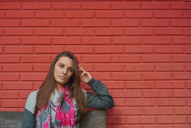 Foto giovane donna pensierosa in piedi contro un muro di mattoni