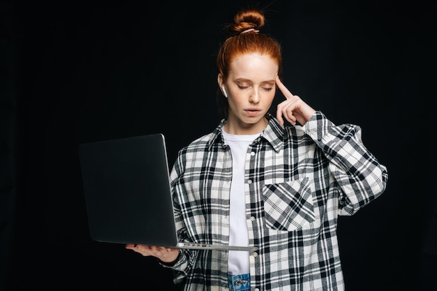 Thoughtful young woman student using laptop computer and looking at screen on isolated background