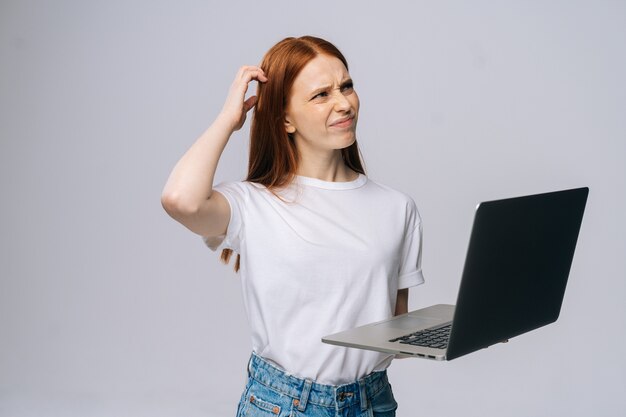 Premurosa giovane studentessa che utilizza il computer portatile e tocca la testa per pensare a nuove idee