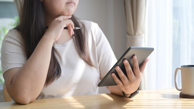 Thoughtful young woman using digital tablet surfing internet at home