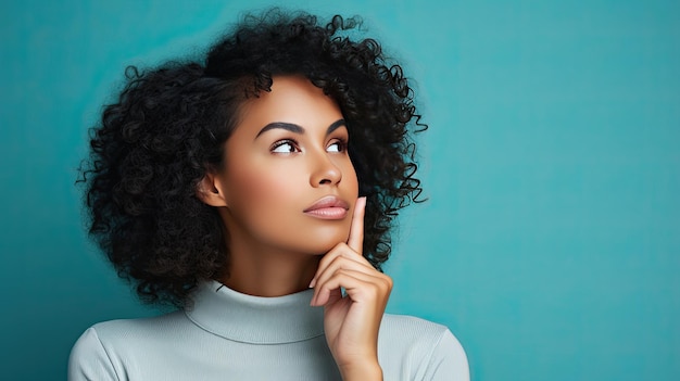 Thoughtful young woman with curly hair holding finger to lips against turquoise background with text space