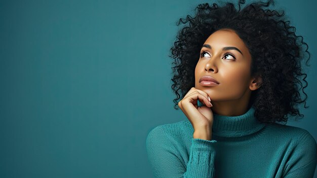 Thoughtful young woman with curly hair holding finger to lips against turquoise background with text space