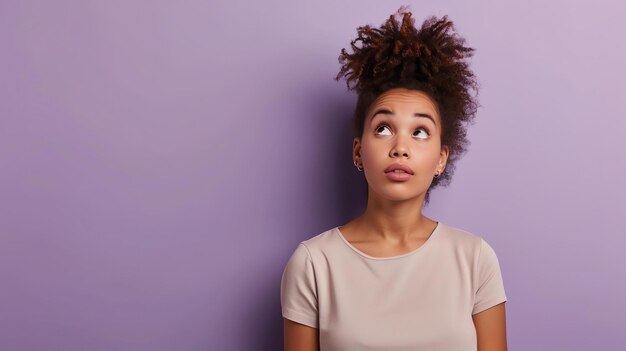 Photo thoughtful young woman with curly hair looking up contemplating something or daydreaming isolated over purple background with copy space