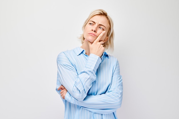 Thoughtful young woman with hand on chin wearing a blue shirt isolated on a white background