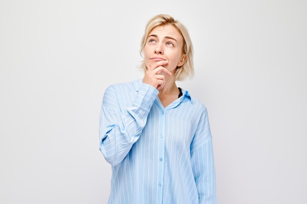 Thoughtful young woman with hand on chin wearing a blue shirt isolated on a white background