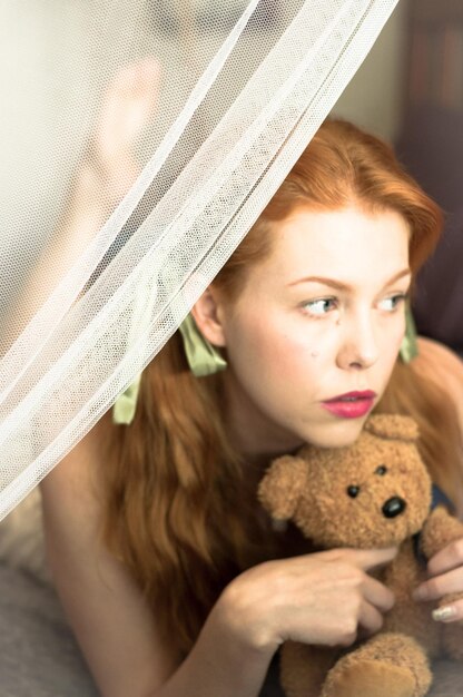 Thoughtful young woman with teddy bear on bed at home