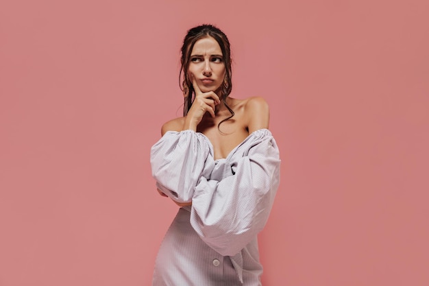 Thoughtful young woman with trendy hairstyle in lilac modern outfit looking away and posing on isolated pink background