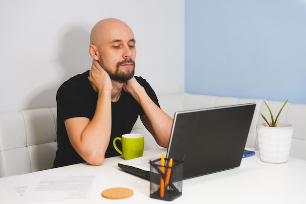 Thouthful bald man with beard in black Tshirt working on his notebook at home side view