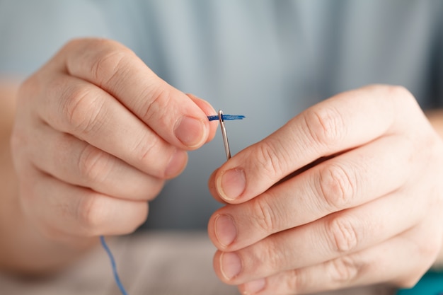 Thread into the needle. Close-up of man pulling thread into the needle